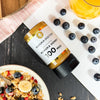 Manuka Doctor Manuka Honey 100 MGO on a table with a bowl of cereal and blueberries.