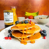 Stack of pancakes with syrup, berries, and Manuka Doctor honey on a plate.