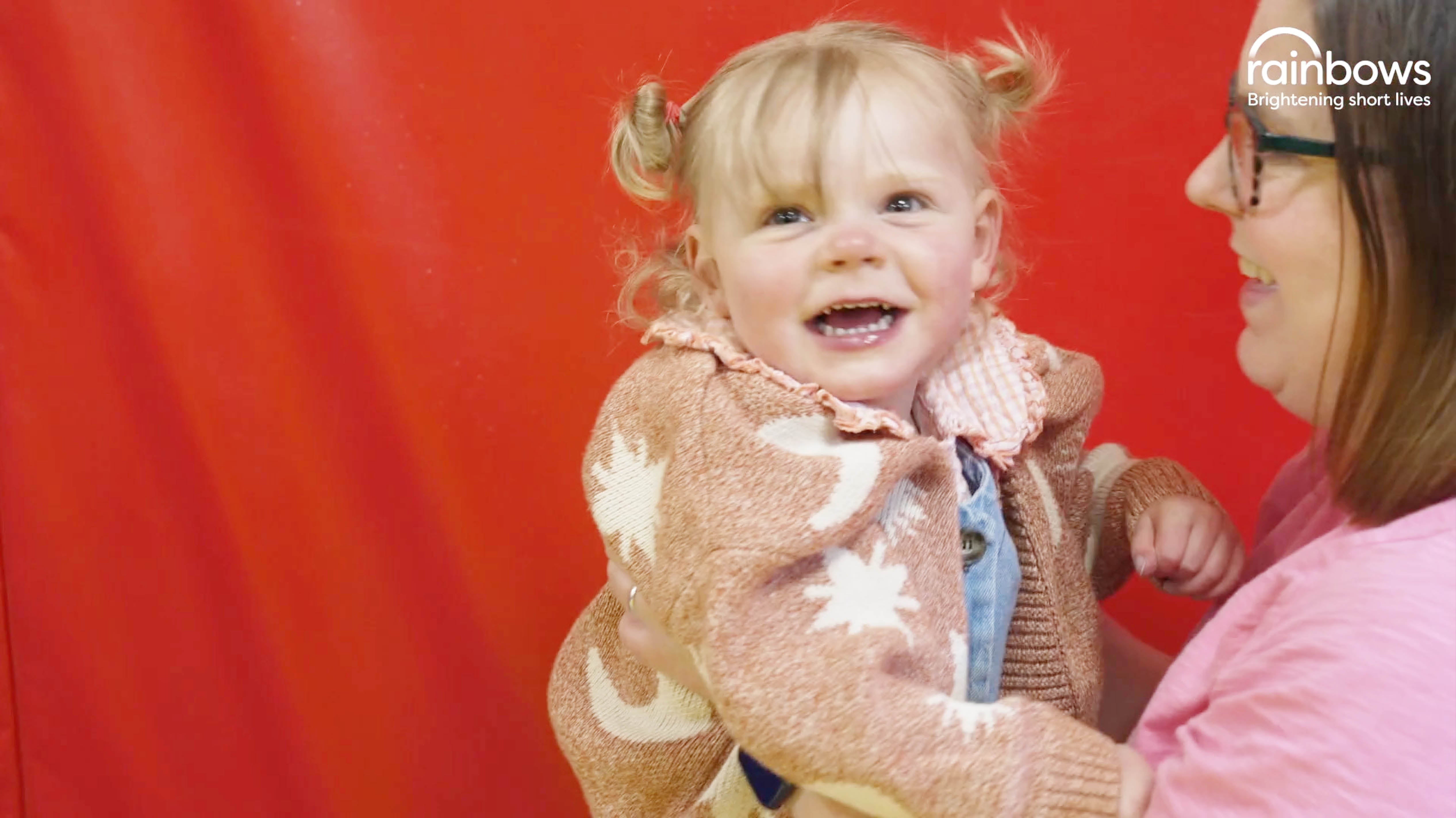 Image of a child smiling with a mother holding her with a red background. 